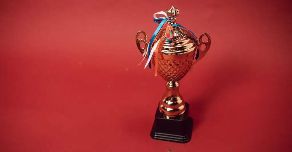 Golden trophy cup with red, blue, and white ribbons on a red backdrop symbolizes achievement and success.
