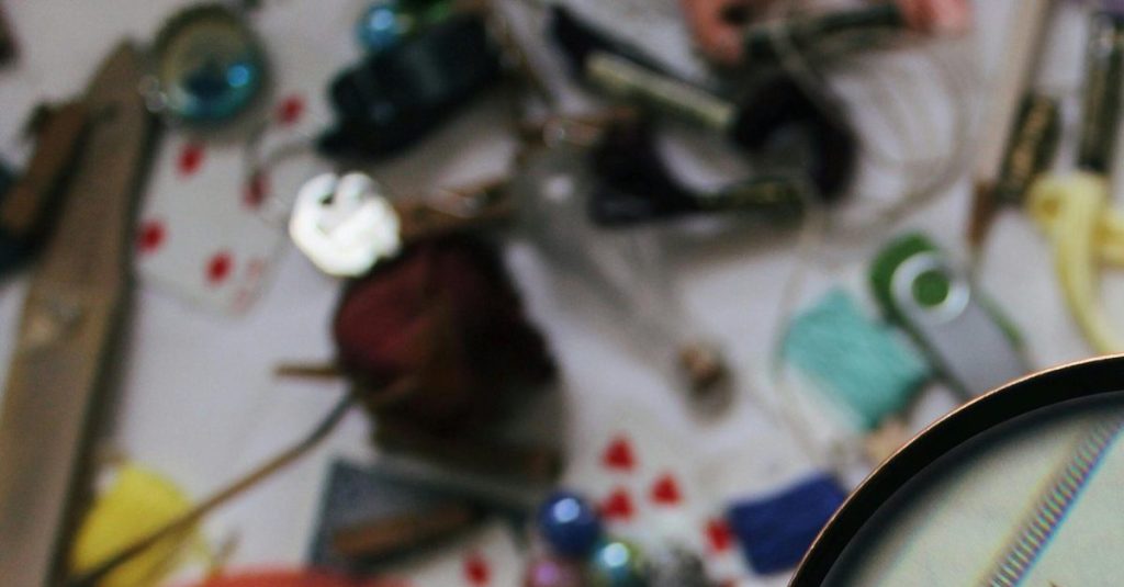 A hand holding a magnifying glass focusing on a twenty dollar bill amidst various scattered objects.