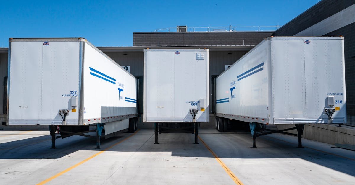 pexels photo 1267325 1267325 Three white cargo trailers parked at an industrial shipping dock under clear blue skies.