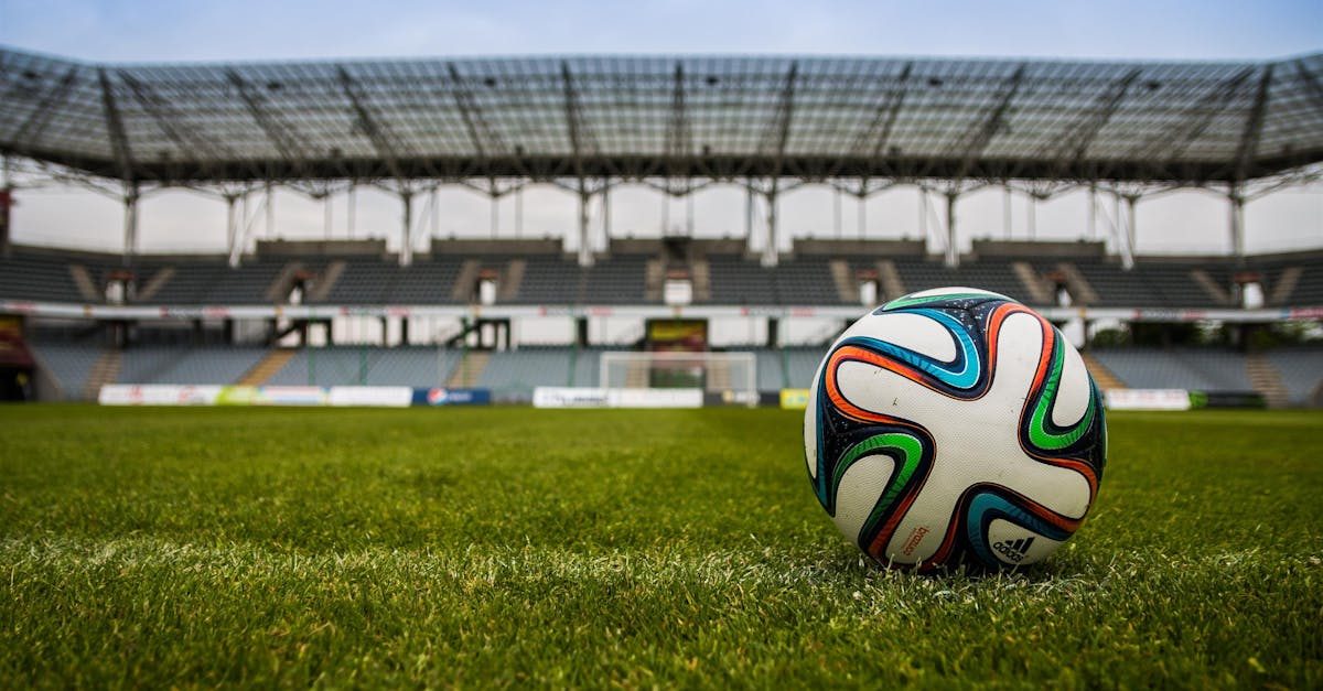 the ball stadion football the pitch 46798 46798 Close-up of a soccer ball on a lush grass field with an empty stadium in the background.